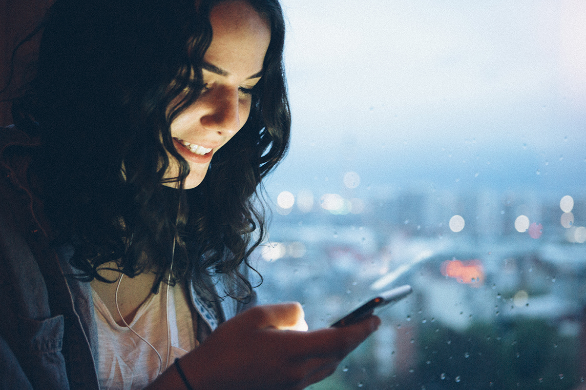woman looking at smartphone with rainy skyline in background