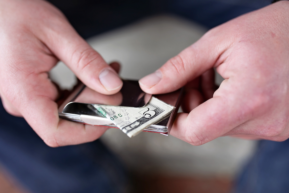 man's hands holding a $5 bill in a money clip.
