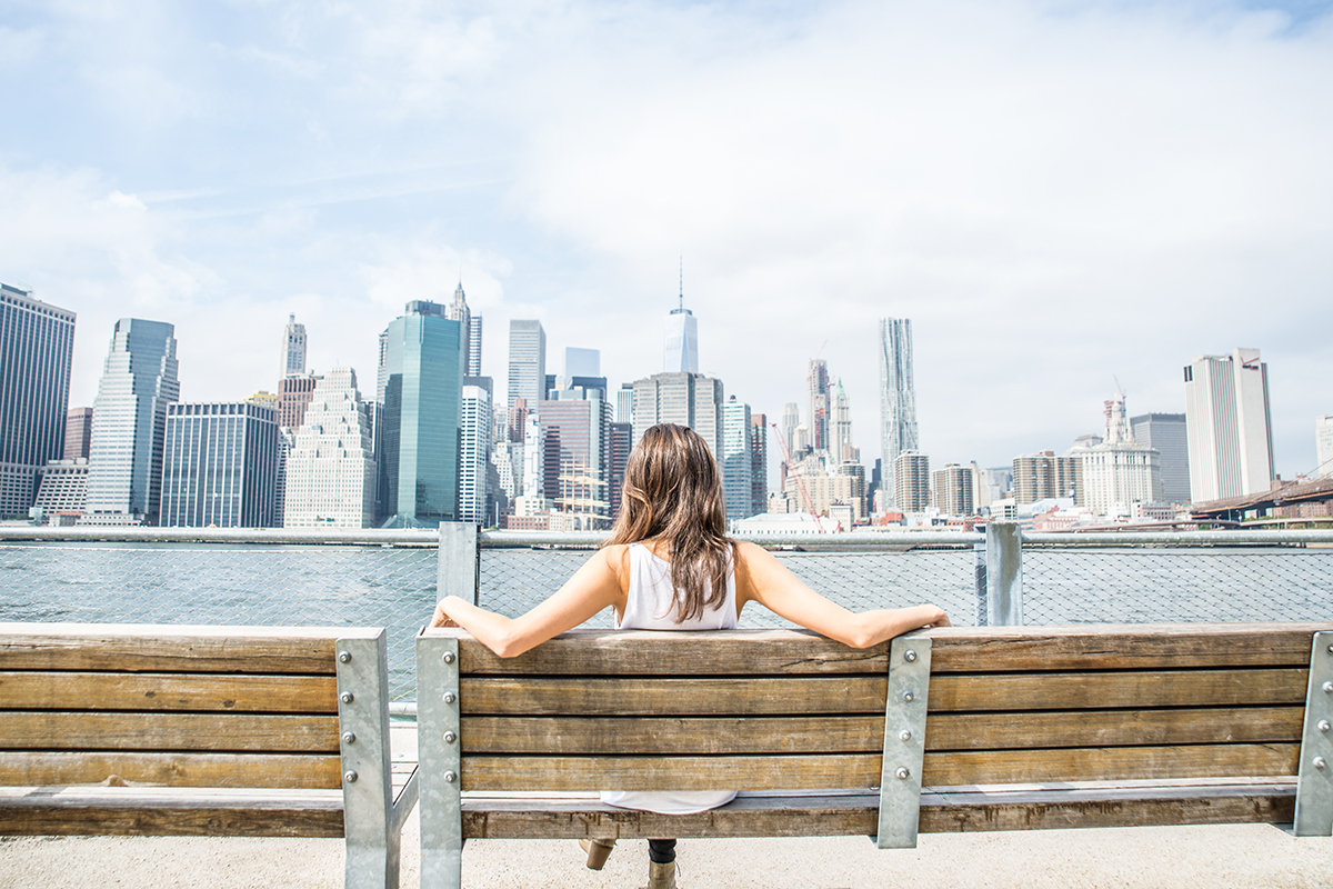 a woman sits on a bench overlooking the skyline of Manhattan in New York.