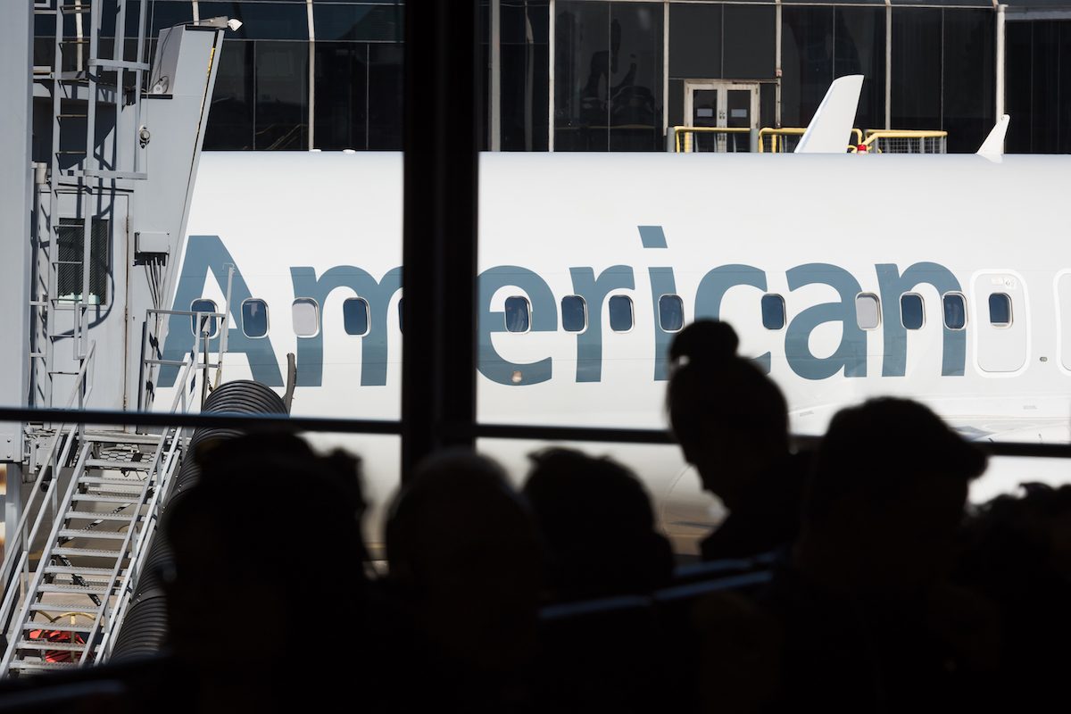 People waiting in Chicagos Ohare International airport late in the day with an American Airlines plane parked at a gate in the background.