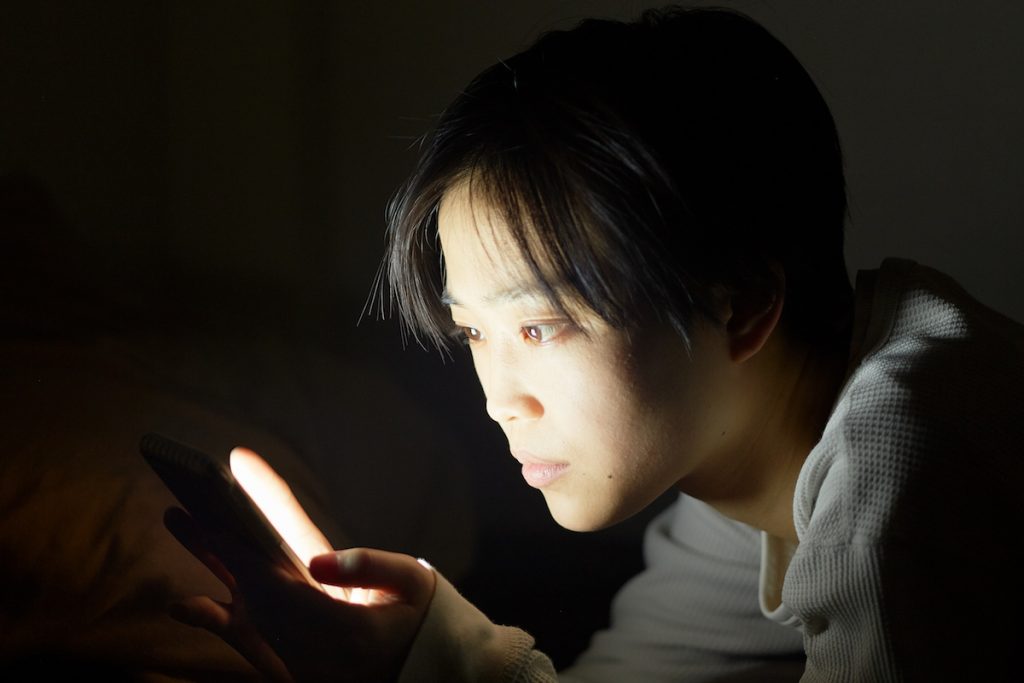 Young woman fiddling her smartphone before bed.