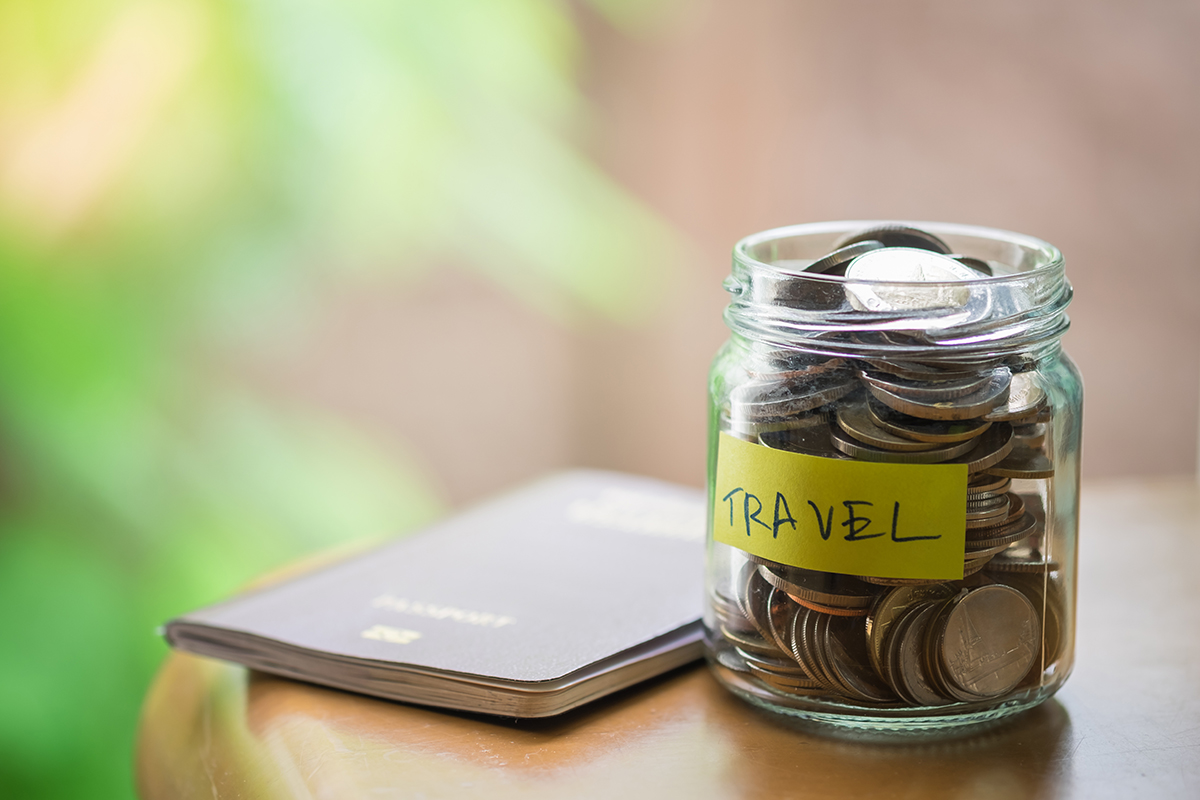 Full of coins in clear bottle with yellow label note with Travel word and passport on wooden table.