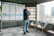 A young man stands by a bulletin board in an office with a view of a city.