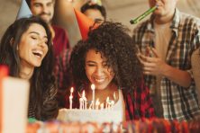 Excited girl ready to blow out candles on cake on birthday party with happy friends.