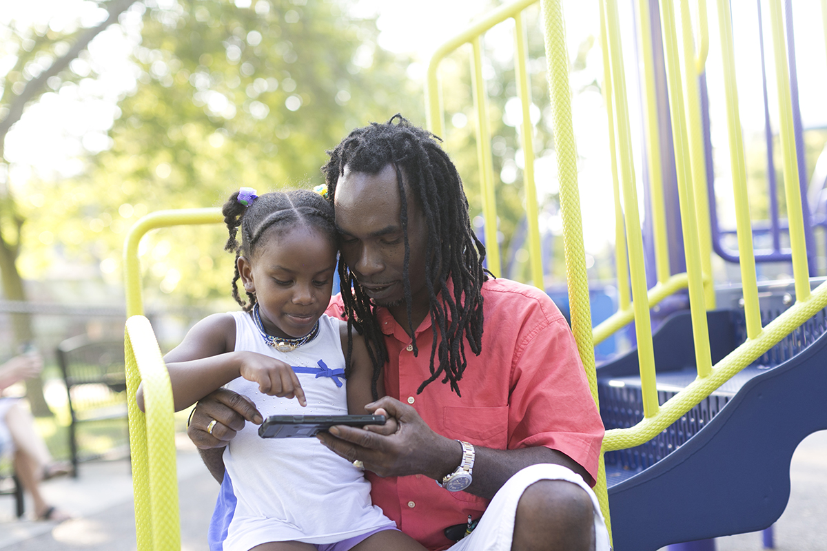 Oneil Campbell shows his 5-year old daughter Anikka how to play the Lucktastic app on his cell phone.