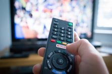 A remote control is held by a hand in front of a TV.