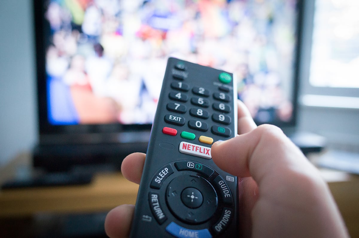 A remote control is held by a hand in front of a TV.