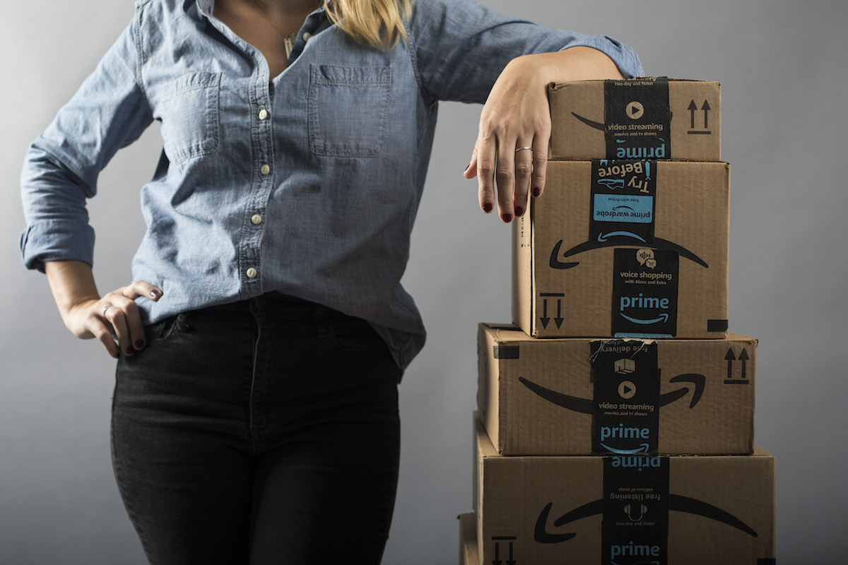 A woman stands next to a tall stack of Amazon shipping boxes.