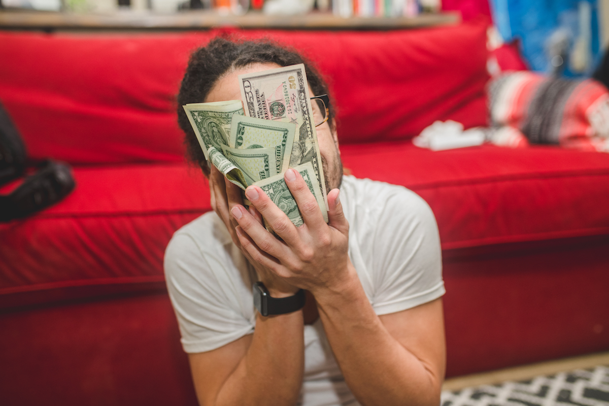 A man sitting in his living room rubs a pile of cash in his face.