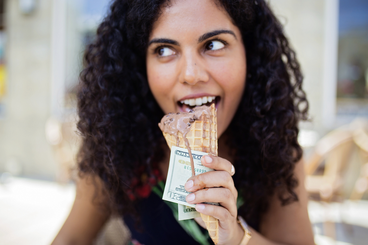 A woman enjoys a chocolate ice cream cone as she holds on to a $20 bill.