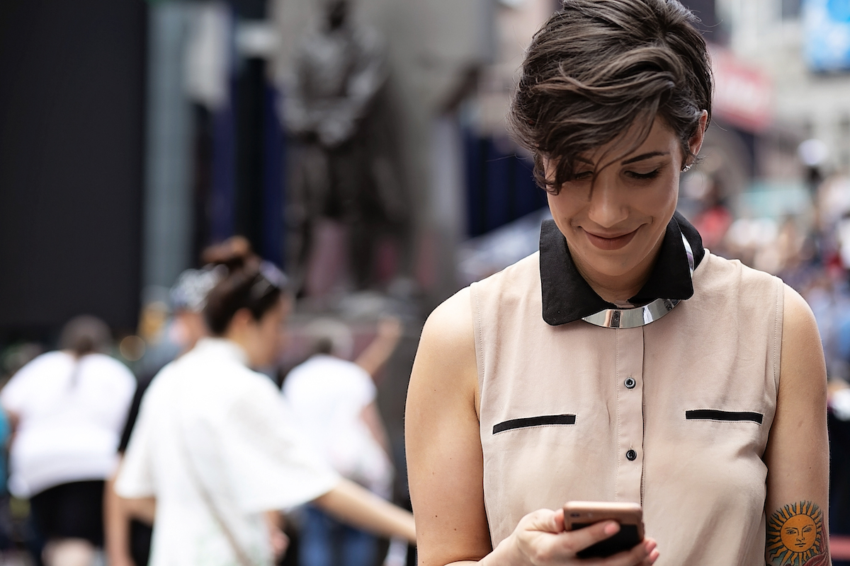 A young woman uses her phone as she walks down a NYC street.