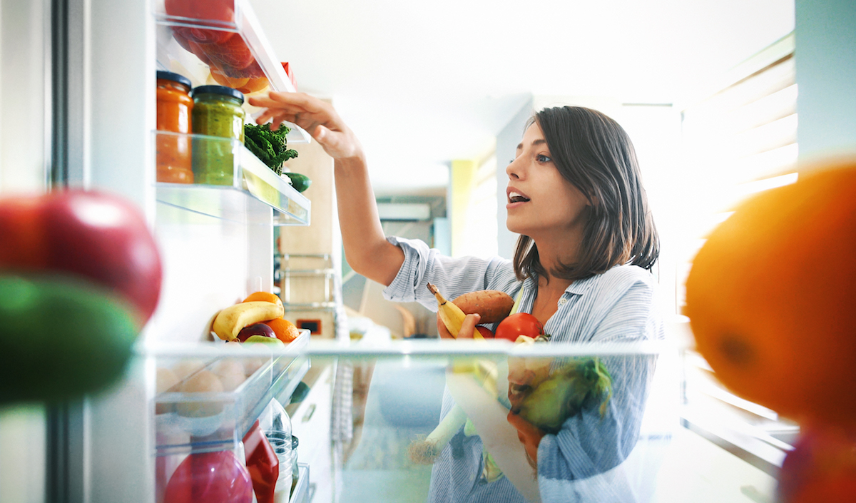 Closeup of a cheerful young woman picking some fruit and veggies from the fridge