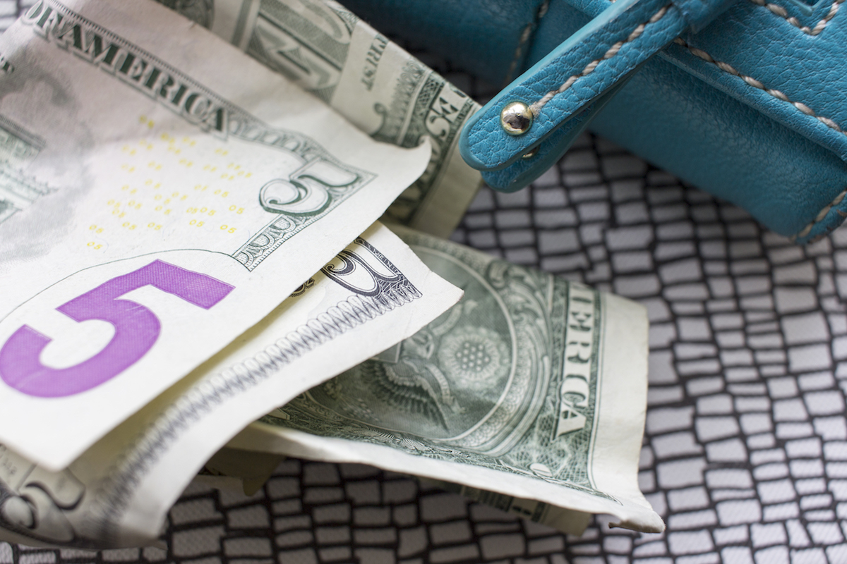 A close up of a $5 bill and a wallet.