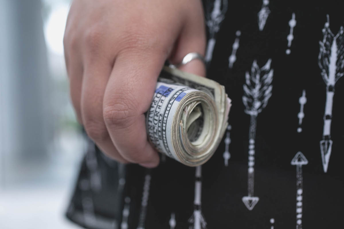 A young woman gripping a rolled up wad of cash.