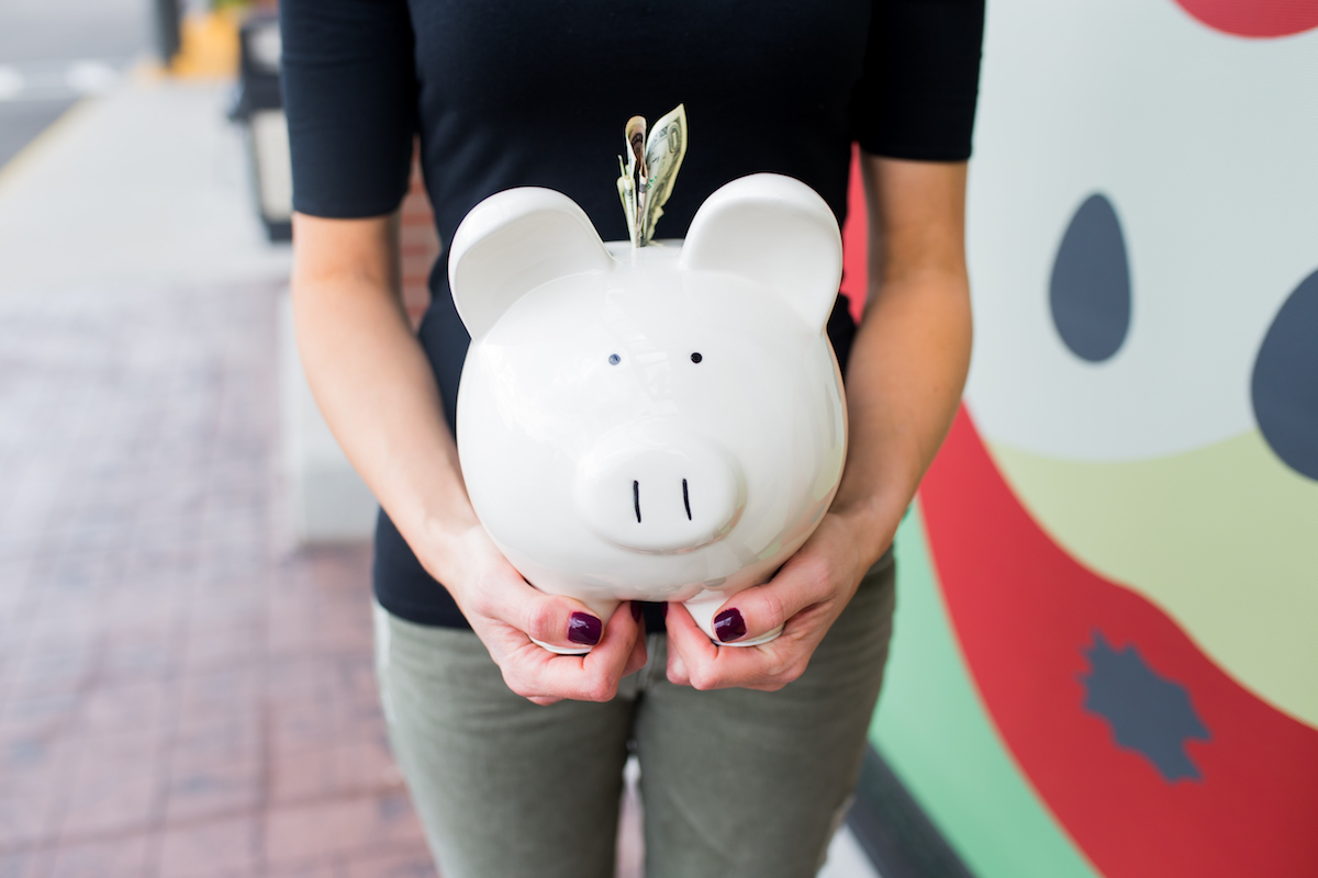 A woman holds her piggy bank, which has dollar bills sticking out of the top opening.