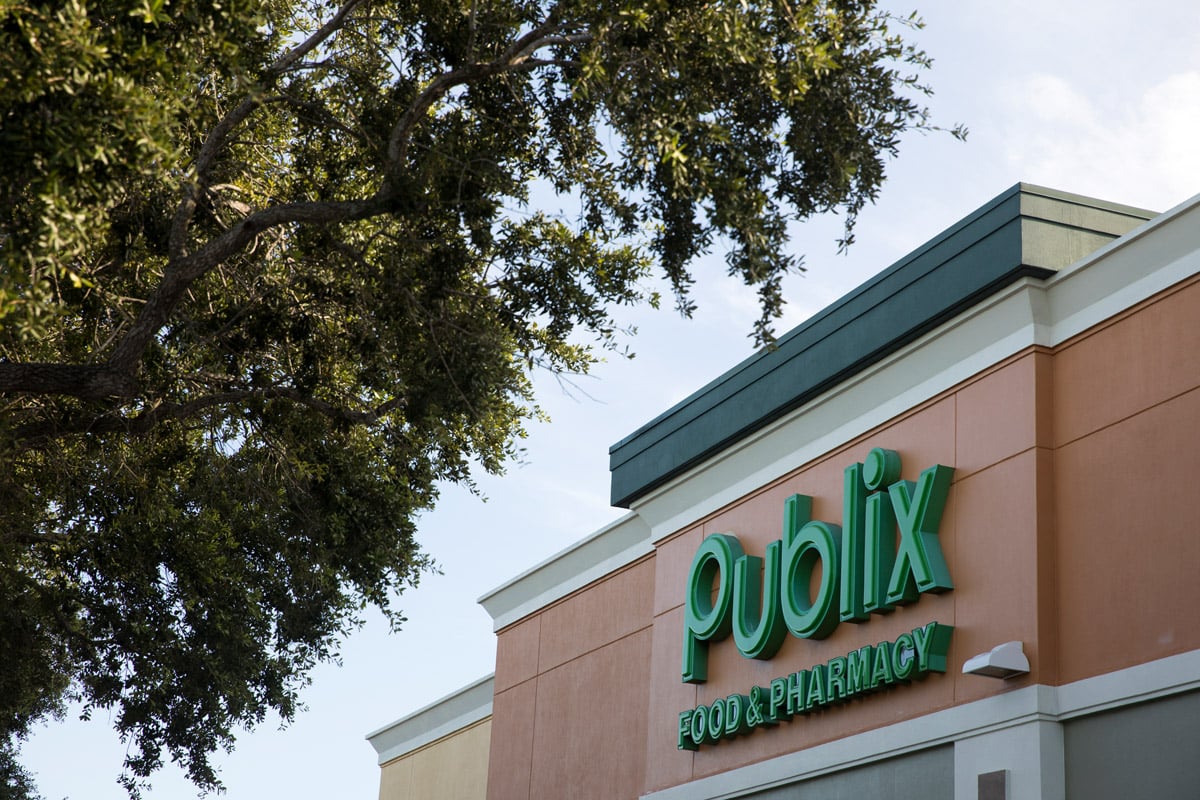 A Publix sign on their shopping building is shown against green trees. 