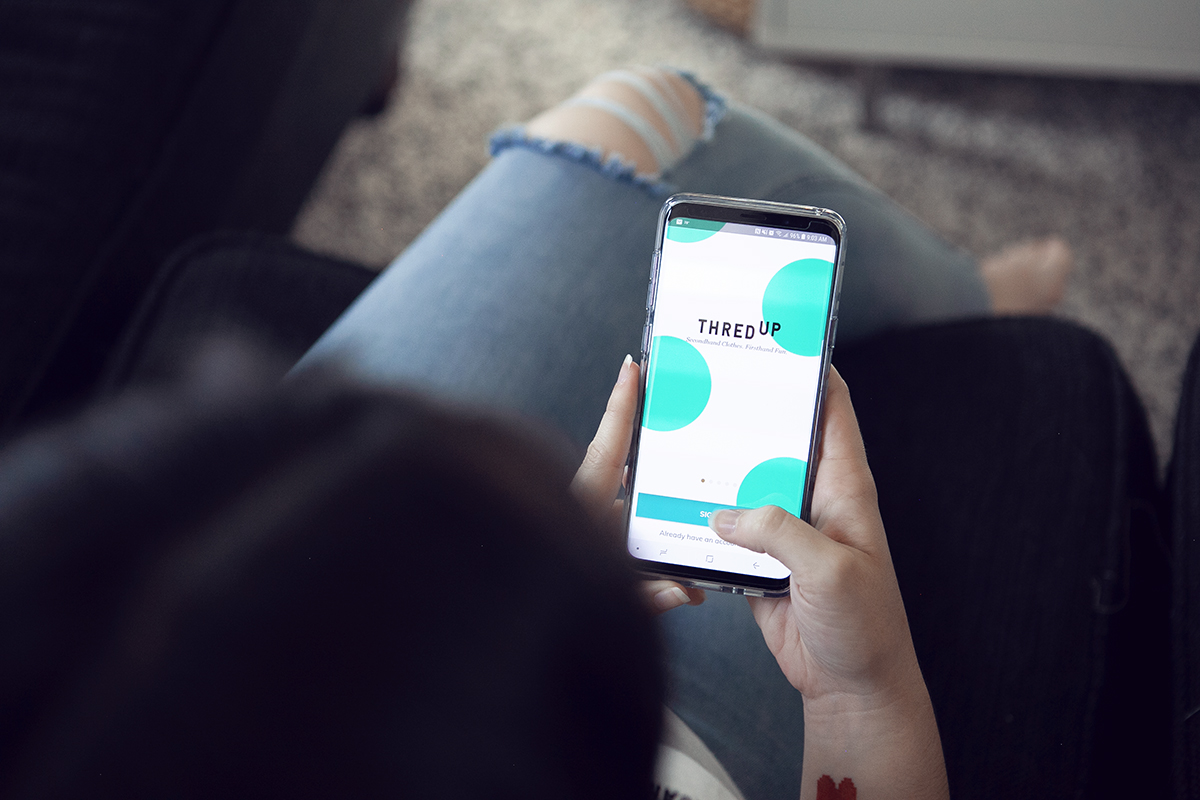Michaela Estes uses the ThreadUp app on her phone while sitting on the couch
