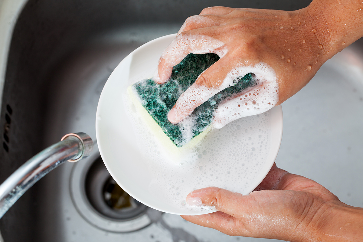 Woman hand washing dishes over the sink in the kitchen.