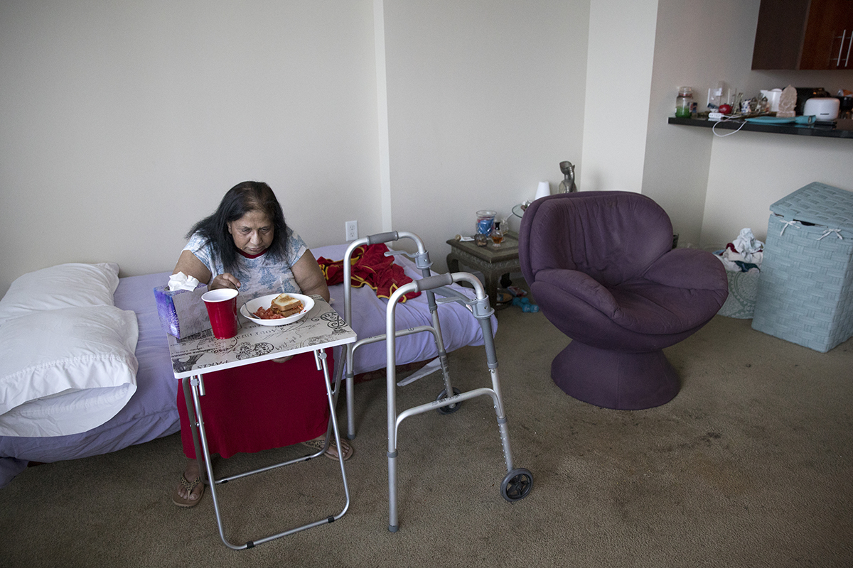 An elderly woman eats lunch in her home that's located in the one bedroom apartment of her daughter's home.