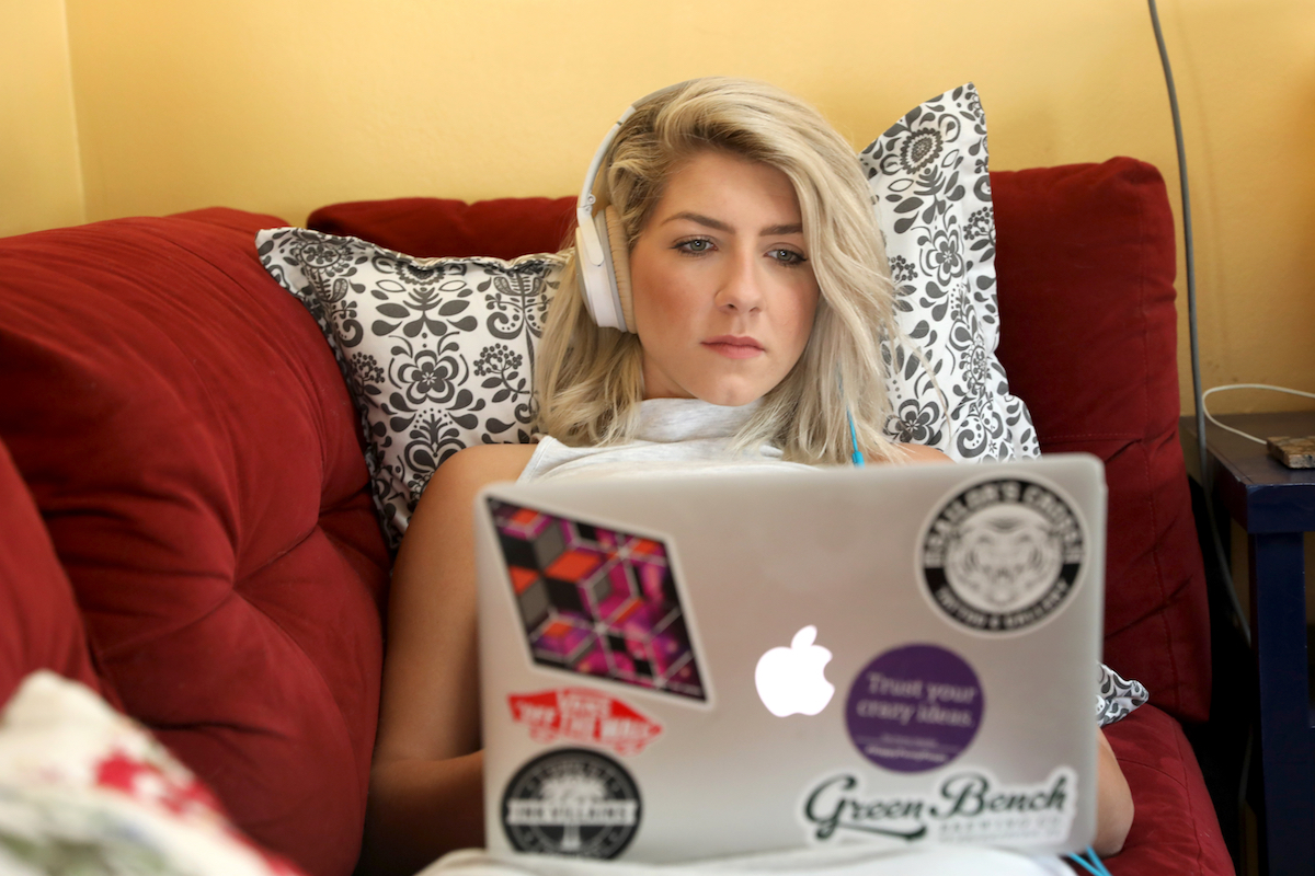 A woman wearing noise cancelling headphones works from home with her laptop on her sofa.