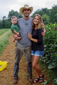 A young couple and their little boy pose for a family photo in a vegetable field on a farm.