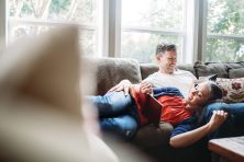 A couple in their 50's relax in their home on the living room couch, enjoying a good book.