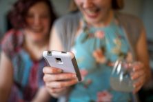 A smiling woman and and another woman look at at mobile phone.