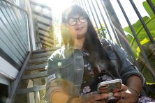 A young woman sitting in the sun looks at her mobile phone.