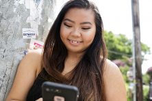 A young woman smiles as she looks at her phone.