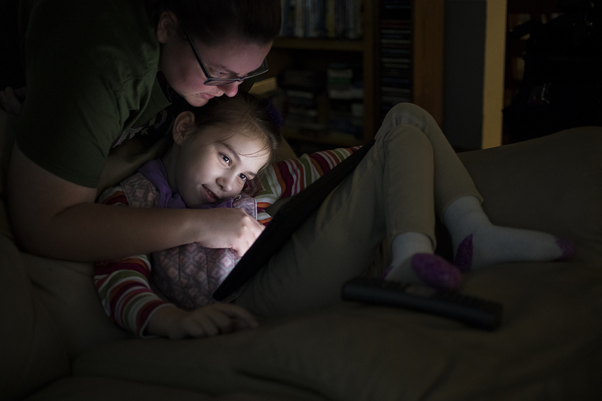 An older sister helps her little sister find a game on her iPad.