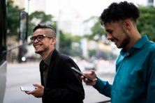 Two business men laugh while holding their phones.