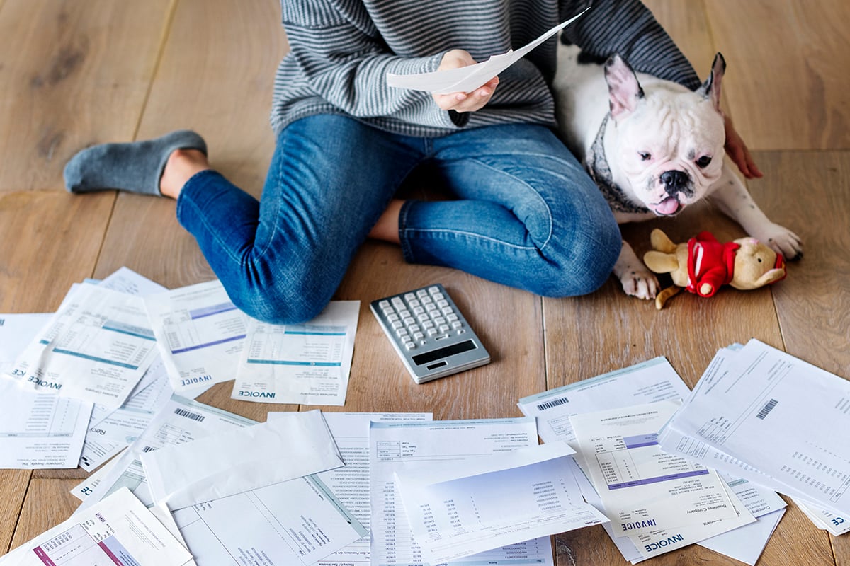 A woman with a dog reviews financial docements spread out on the floor.