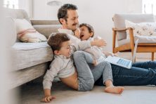 A dad works on his laptop as his two sons pile on top of him.