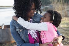 A woman hugs her young daughter next to a lake