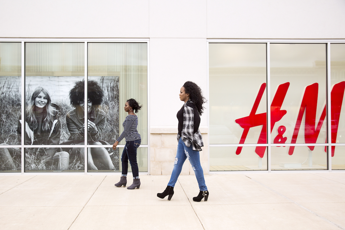 Two women walk past a store at an outdoor mall.