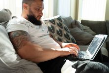 Man with tattoos working on his laptop in his apartment