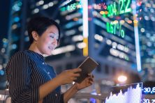Asian businesswomen checking stock market data on tablet before Hong Kong financial display board