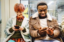 Two people smile as they look on their phones on the public bus.