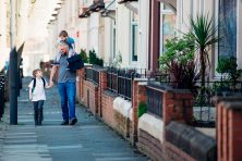 A man walks down the street with his two young sons.