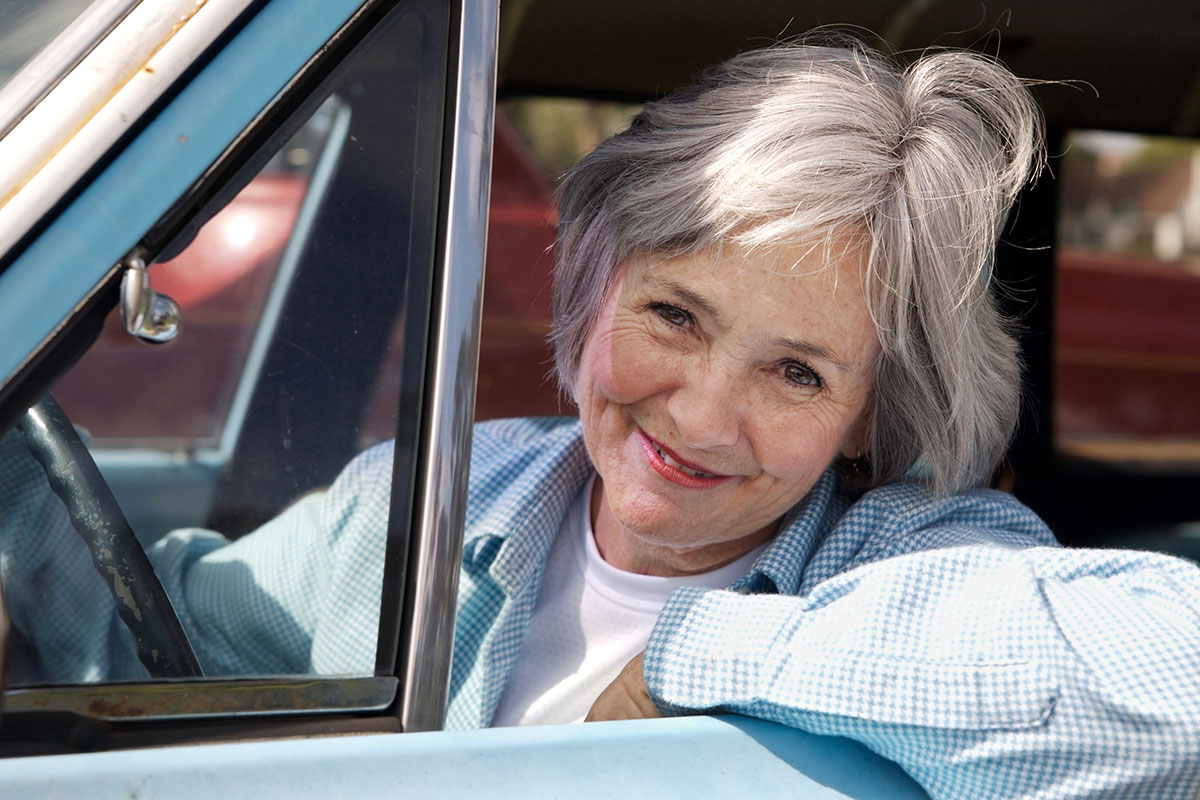 An smiling older woman drives a car.