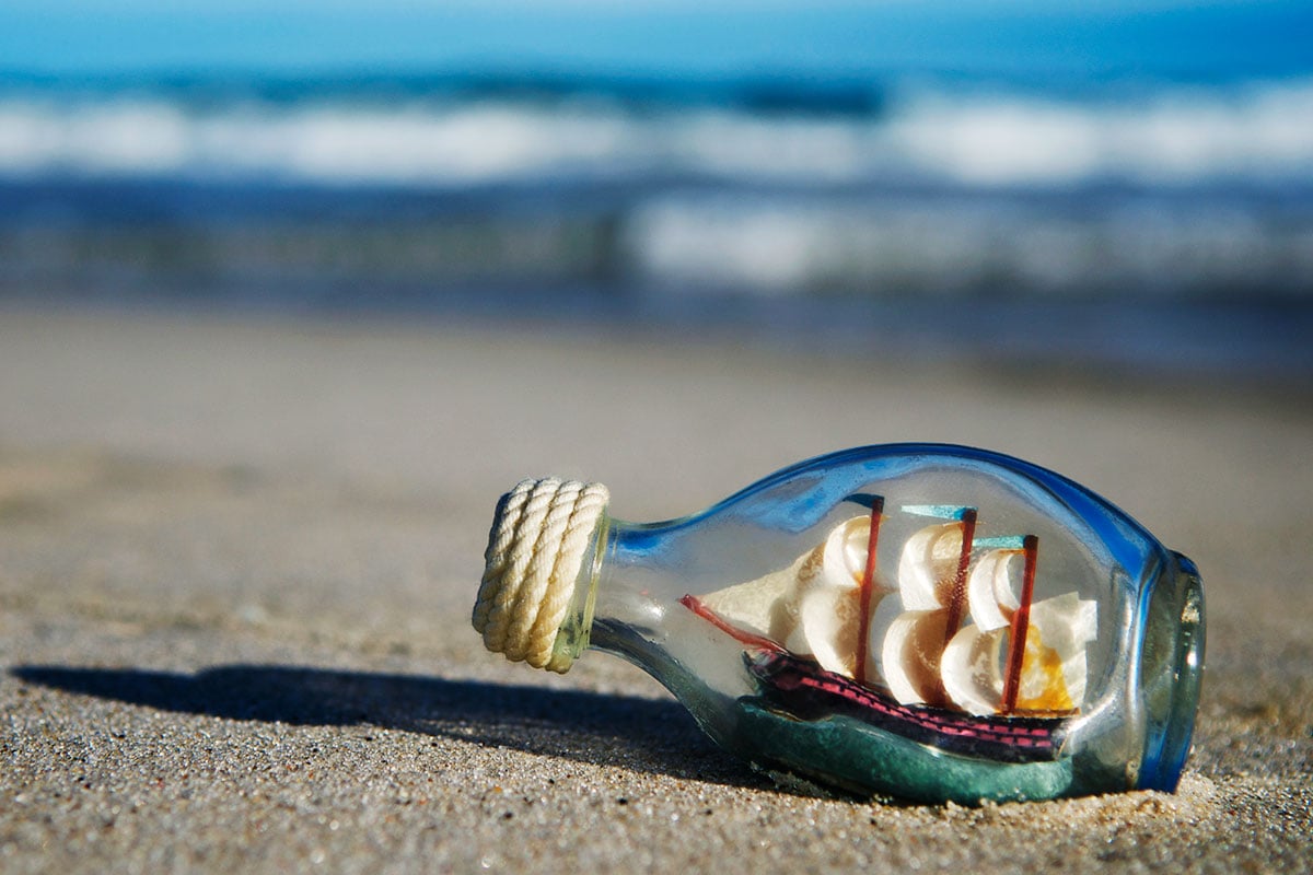 A ship in a bottle rests on the sand at a beach.