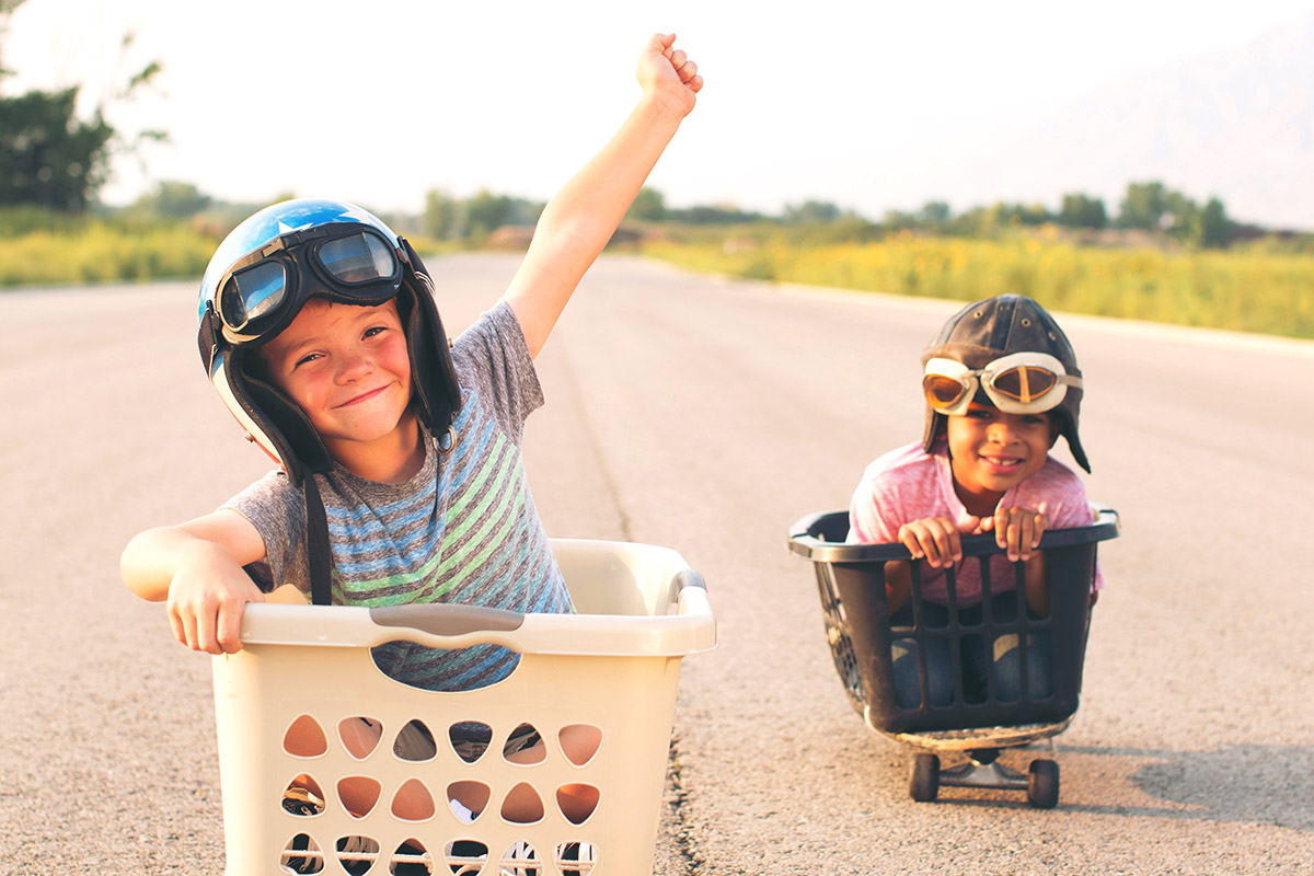 Two boys race in laundry baskets on skateboards.