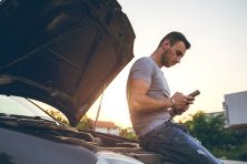 Young man is text messaging, standing next to a broken down car