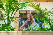 A woman sits between plants on the back porch of a coliving space.