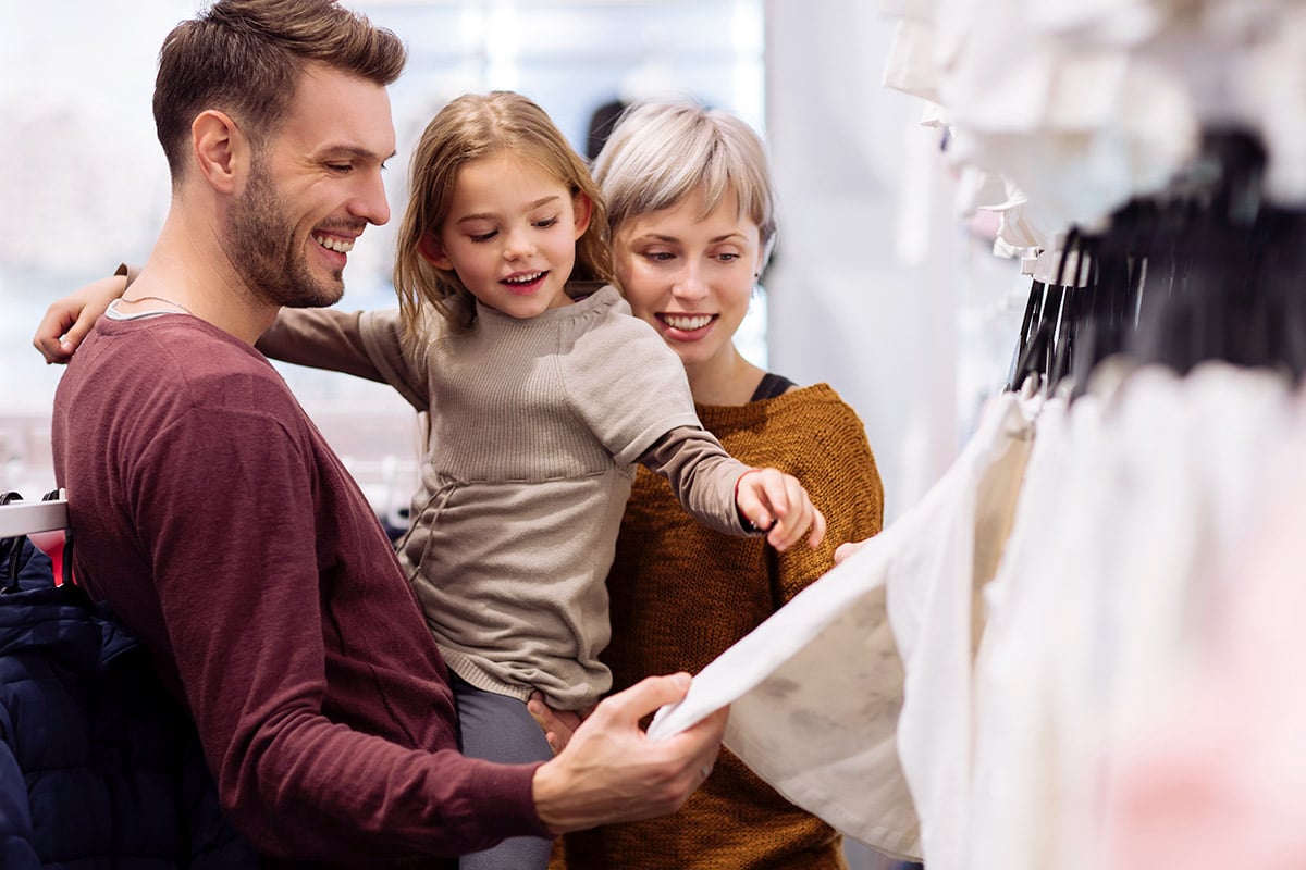 parents shop for clothes with theiir young daughter.