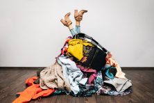 A woman's legs appear upside down after diving into a pile of clothes. used clothes, clothes, boots, sweater and blouse.