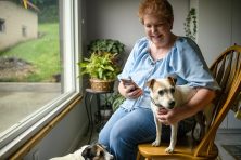 A woman sits with her phone and dog.