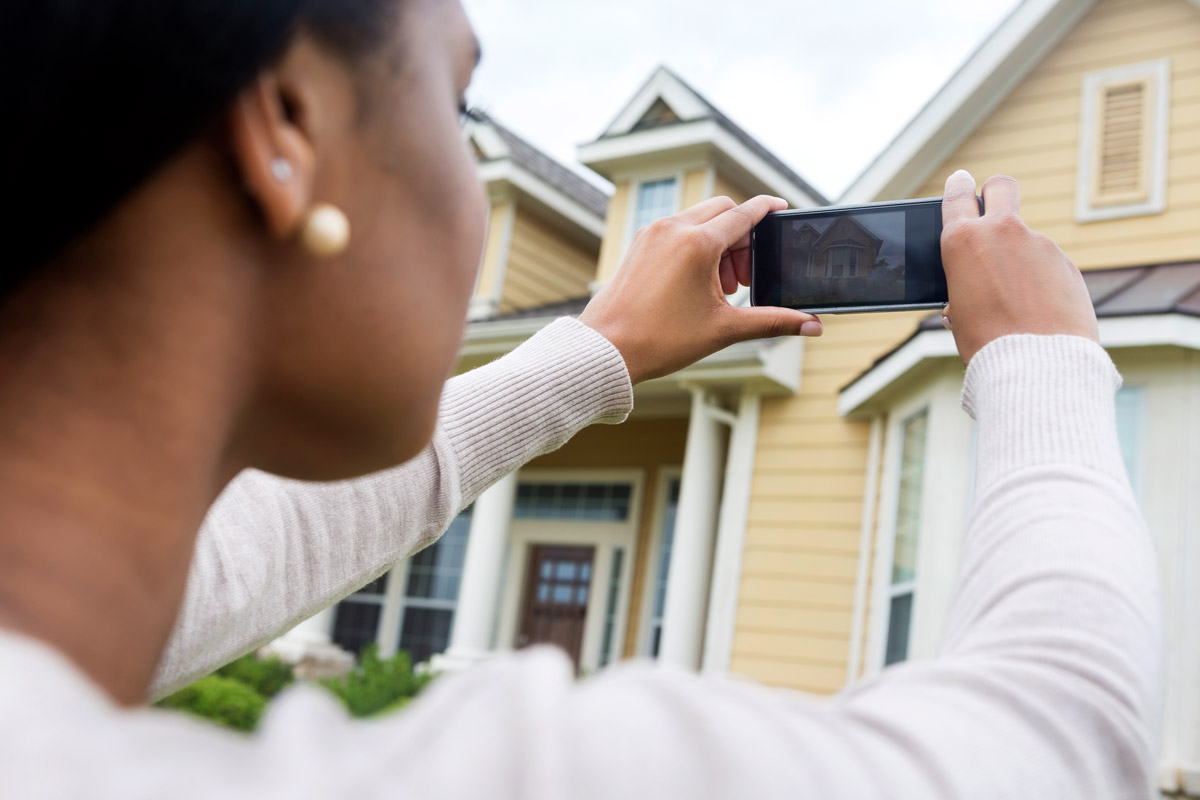 A woman photographs the outside of her home.
