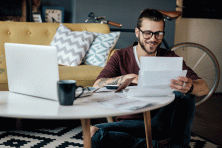 A male student sits in his living room looking at a sheet of paper.