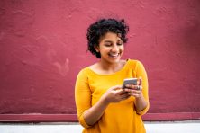 A woman wearing a yellow sweater smiles at her phone.